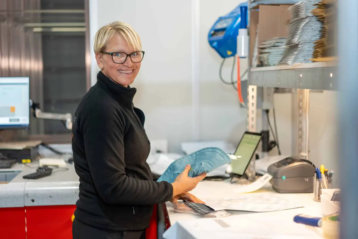 Medarbeider med en vare i hånden og et nettbrett ved pakkestasjonen