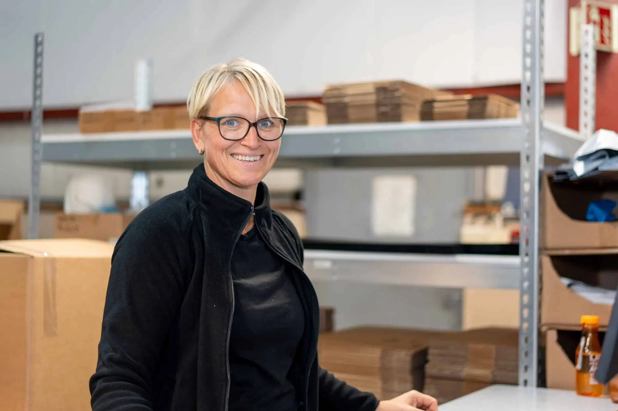 Smilende medarbeider ved reolene på pakkelageret